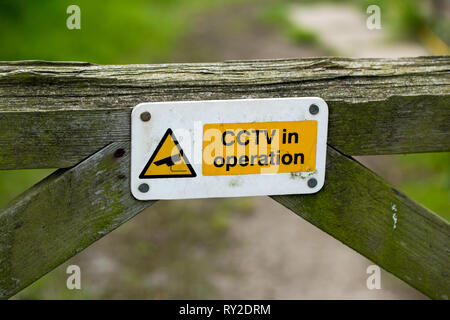 Warning sign on a wooden, timber, farm field gate. CCTV in operation. On a locked farm gate. Registering an  owners fear of domestic livestock theft.  Stock Photo
