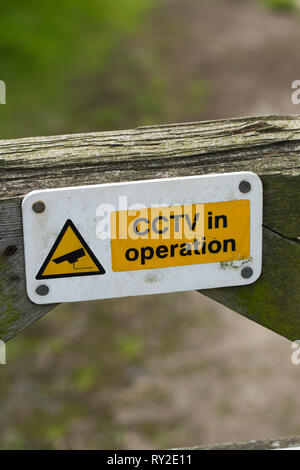 Warning sign on a wooden, timber, farm field gate. CCTV in operation. On a locked farm gate. Registering an owner's fear of domestic livestock theft. Stock Photo