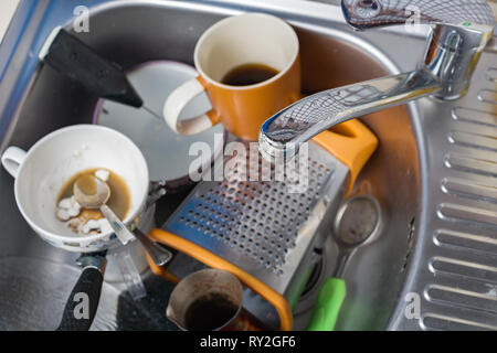 A pile of dirty and unwashed dishes in the sink close-up. Leftover coffee in glasses. Stock Photo