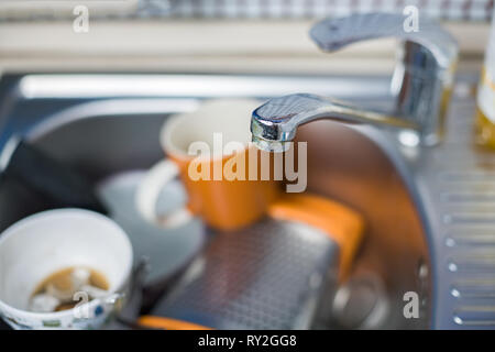 A pile of dirty and unwashed dishes in the sink close-up. Leftover coffee in glasses. Stock Photo