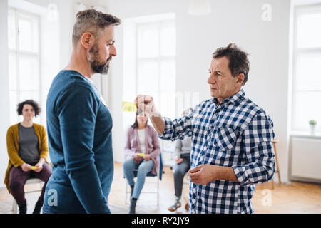 A counsellor putting an adhesive note with the word angry on client during group therapy. Stock Photo