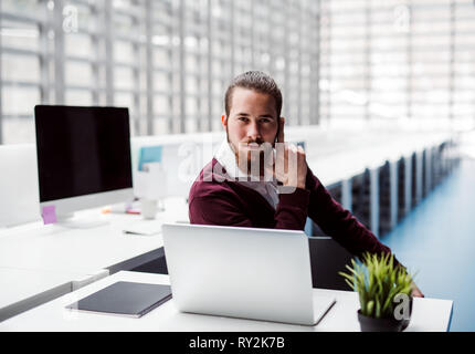 A young serious businessman with laptop in office, looking at camera. Stock Photo