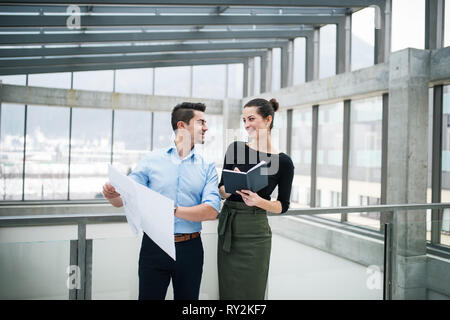 Two young male and female architects with blueprints standing in office, talking. Stock Photo