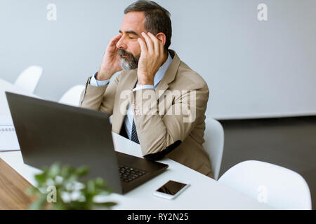 Handsome senior businessman gray hair working on laptop in modern office and having headache Stock Photo