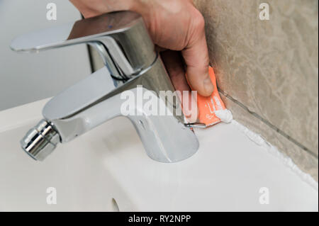 Worker smoothing silicone sealant between the bidet and the wall using a spatula. Stock Photo