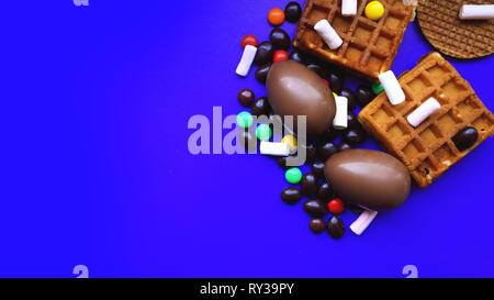 Delicious chocolate easter eggs, waffles, sweets on dark blue background Stock Photo