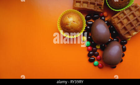 Delicious chocolate easter eggs, waffles, sweets on orange background Stock Photo