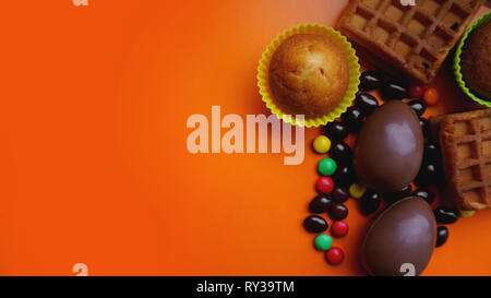 Delicious chocolate easter eggs, waffles, sweets on orange background Stock Photo