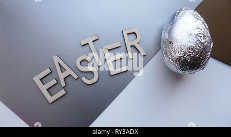 Egg in foil on silver background. Easter concept banner. With text Easter Stock Photo