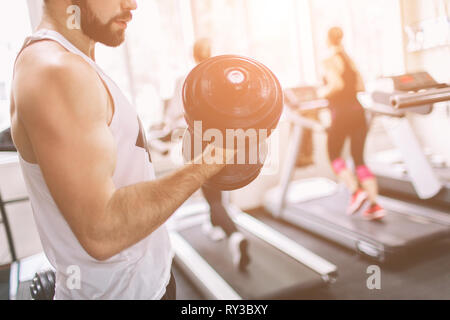 Muscular Bearded man during workout in the gym. Athlete muscular bodybuilder in the gym training biceps with dumbbell. Indoor fitness Stock Photo