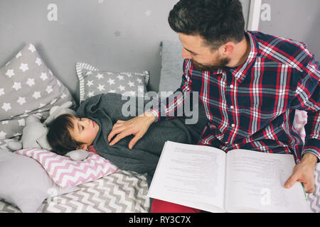 Father reading a book to his daughter while lying on the bed in bedroom Stock Photo