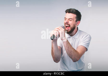 Boy Rocking Out. Image of a handsome man singing to the microphone, isolated on light. Emotional portrait of an attractive guy on a gray background Stock Photo