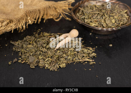 Composition lot of pieces of dry green tea with wooden scoop on grey stone Stock Photo