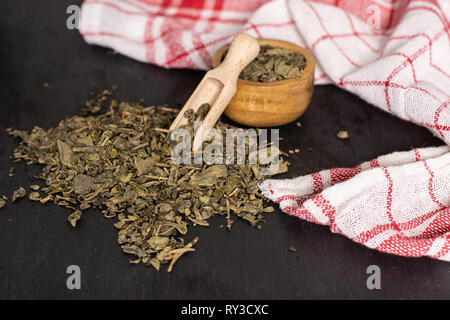 Composition lot of pieces of dry green tea with wooden scoop on grey stone Stock Photo