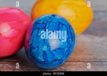 three colored easter eggs on a brown wooden surface Stock Photo
