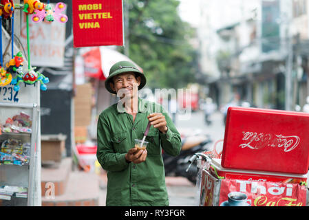 Happy man drinking an  iced coffee in green uniform in Hanoi, Vietnam. Vietnamese smiling man with a refreshment Stock Photo