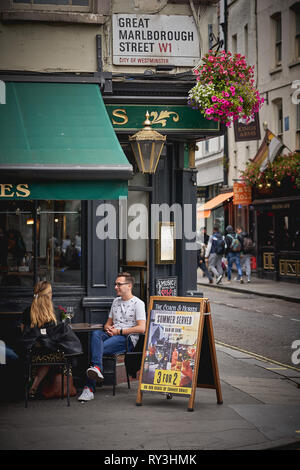 London, UK - August, 2018. Young people having drinks outside a bar coffee shop in Soho, central London. Stock Photo
