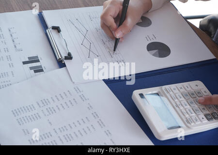 Female working in office, studying using calculator and writing something with documents and chart on table. Stock Photo