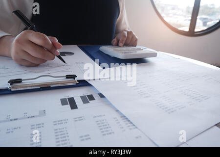 Female working in office, studying using calculator and writing something with documents and chart on table Stock Photo