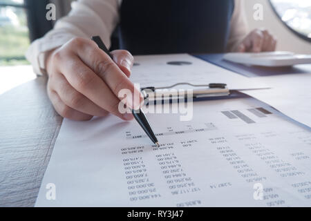 Female working in office, studying using calculator and writing something with documents and chart on table Stock Photo