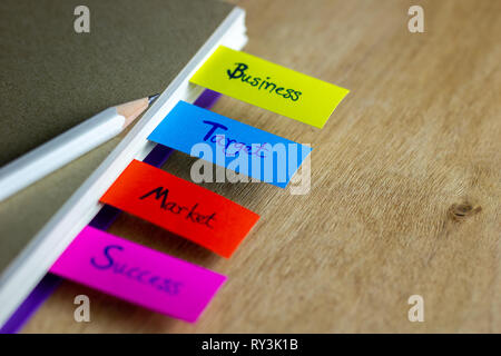 Colorful bookmarks are written for business, target, market, success, and have a white pencil put on a brown book cover. Concept of business. Stock Photo