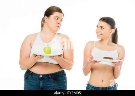 happy slim woman holding plate with doughnut and looking at sad overweight woman with green apple on plate isolated on white Stock Photo