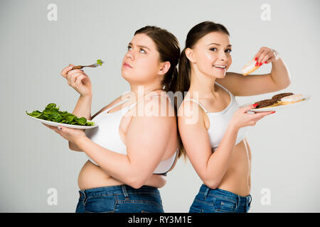 happy slim woman eating doughnuts while sad overweight woman eating green spinach leaves Stock Photo