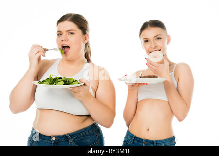 slim woman eating doughnuts while overweight woman eating green spinach leaves isolated on white Stock Photo