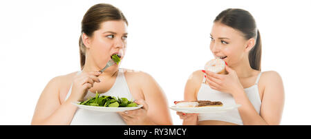 slim woman eating doughnuts and looking at overweight woman eating green spinach leaves isolated on white Stock Photo