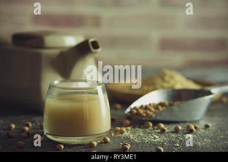 Soymilk in the glass and the kettle is placed beside. Soybean powder is crushed in a wooden dish and has scattered soy beans on the table in morning l Stock Photo