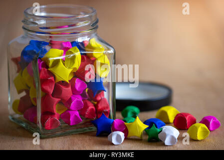 Multicolor paper star in square glass bottle on wooden table with morning sunlight. Stock Photo