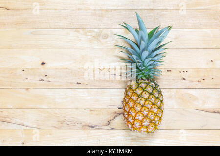 Single whole pineapple with green leaves on the wooden texture background. Top view. Stock Photo