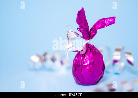 Easter greeting card with candies colored purple egg bunny ears on blue serpentine background. Minimal style, trendy purple colors Stock Photo