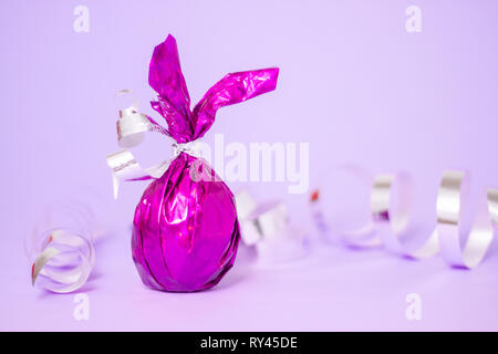 Easter greeting card with candies colored purple egg bunny ears on violet serpentine background. Minimal style, trendy purple colors Stock Photo