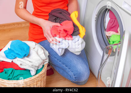 Young woman loads the laundry in the washing machine from the laundry basket before washing. Stock Photo