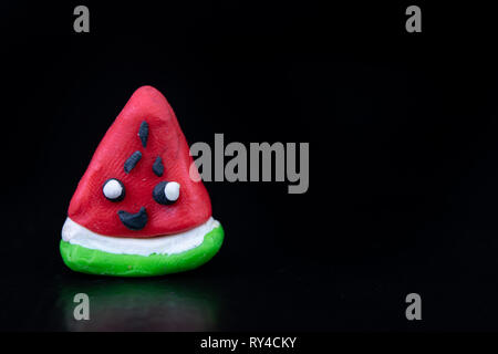 Plasticine figurines on a dark wooden table. Watermelon fruit imitation. Dark background. Stock Photo
