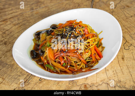 Noodles with vegetables. Mushrooms, zucchini, peppers, carrots in a sweet-sour sauce. Sprinkled with white and black sesame seeds. Stock Photo
