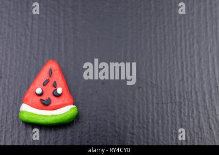 Plasticine figurines on a dark wooden table. Watermelon fruit imitation. Dark background. Stock Photo