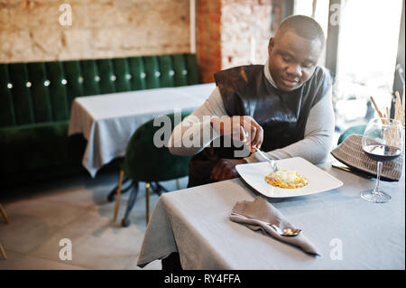 African man in black traditional clothes sitting at restaurant and eat pasta. Stock Photo
