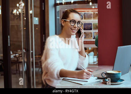 Woman entrepreneur working from cafe and talking on mobile phone Stock Photo