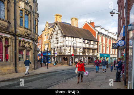people shoppers shopping on the high Street in the Shropshire market town of Oswestry with a view of the black and white half timbered Llwyd Mansion. Stock Photo