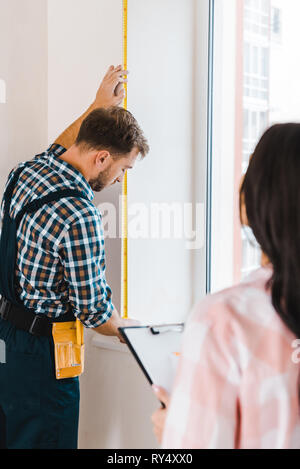 handyman measuring window with measuring tape near female client Stock Photo