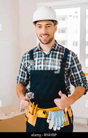 cheerful handyman holding wrench and showing thumb up Stock Photo