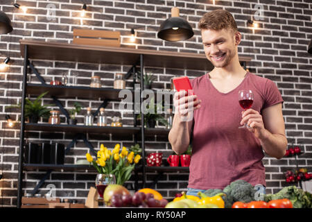 Man holding smartphone and glass of wine waiting for girlfriend at home Stock Photo