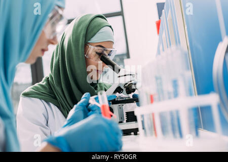 selective focus of female muslim scientist looking through microscope in chemical laboratory Stock Photo