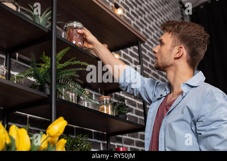 Handsome young bearded man putting jar with spices on the shelf Stock Photo