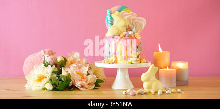 On-trend Easter theme candy land drip cake decorated with lollipops, candy eggs and white chocolate bunny in party table setting. Stock Photo