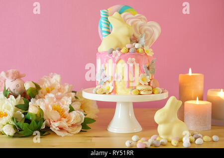 On-trend Easter theme candy land drip cake decorated with lollipops, candy eggs and white chocolate bunny in party table setting. Stock Photo