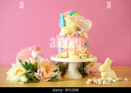 On-trend Easter theme candy land drip cake decorated with lollipops, candy eggs and white chocolate bunny in party table setting. Stock Photo