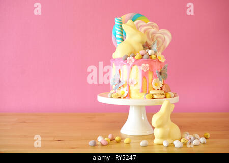 On-trend Easter theme candy land drip cake decorated with lollipops, candy eggs and white chocolate bunny in party table setting. Stock Photo